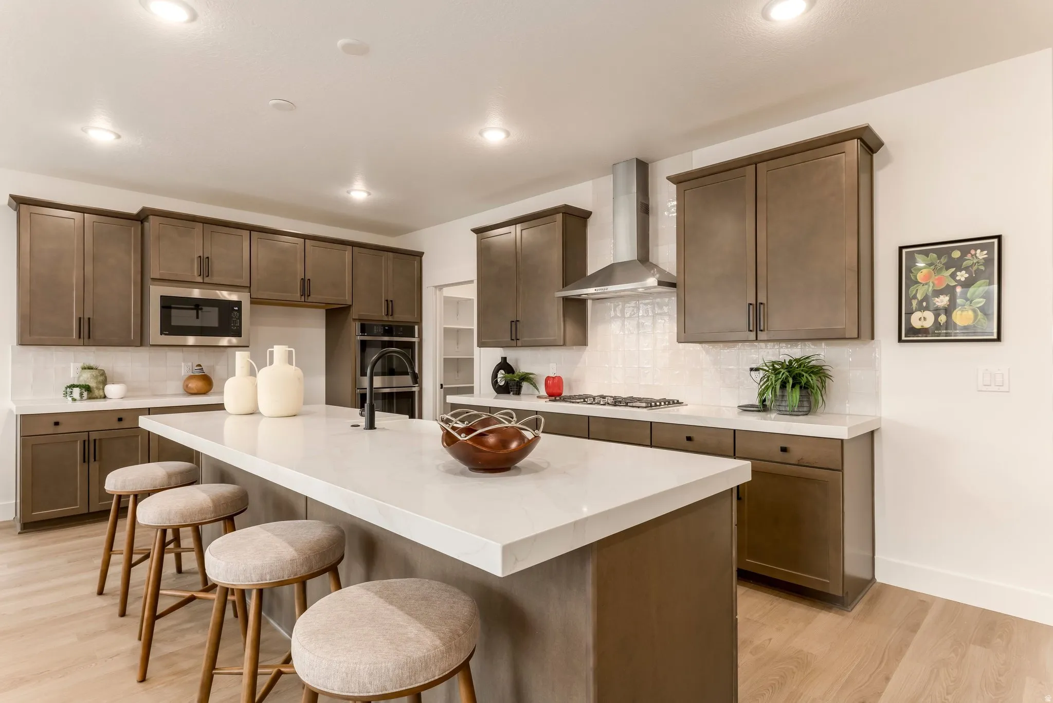 Kitchen featuring a kitchen bar, light wood finished floors, a kitchen island with sink, stainless steel appliances, and light stone counters