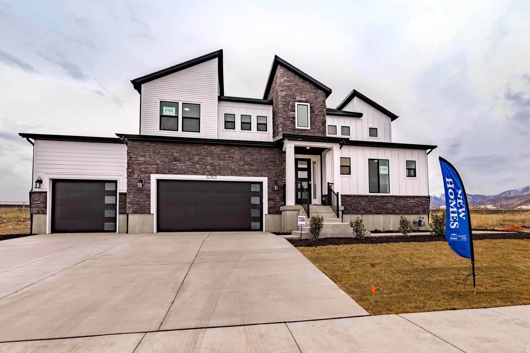 View of front facade featuring stone siding, board and batten siding, concrete driveway, an attached garage, and a front lawn