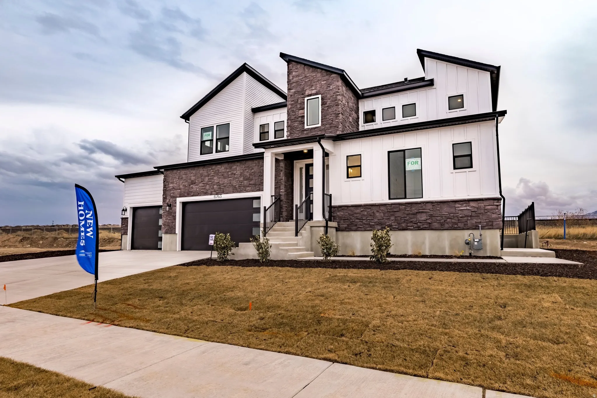 View of front of home with stone siding, board and batten siding, an attached garage, and a front lawn