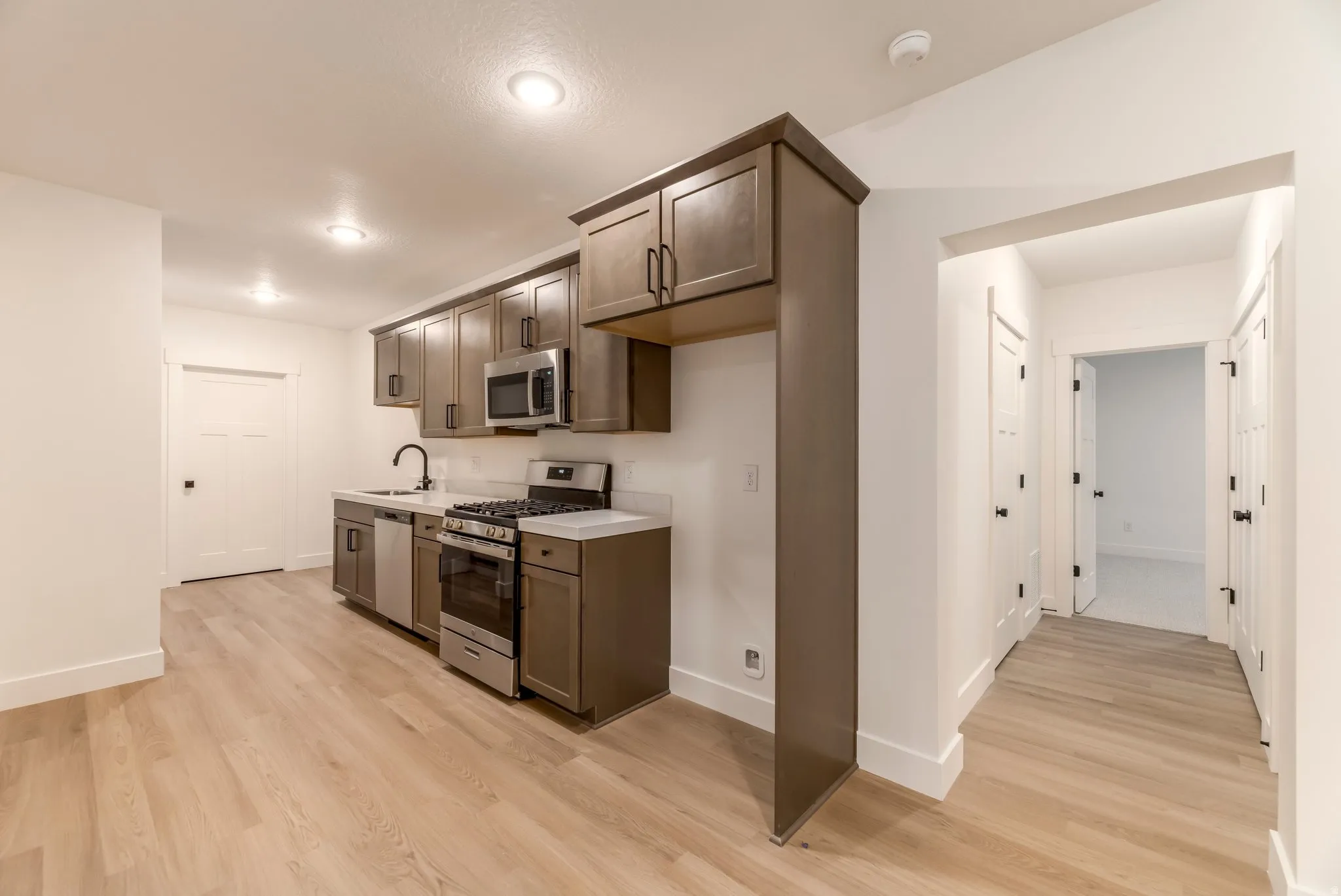 Kitchen with stainless steel appliances, light countertops, dark wood finish cabinets, and light wood-style flooring