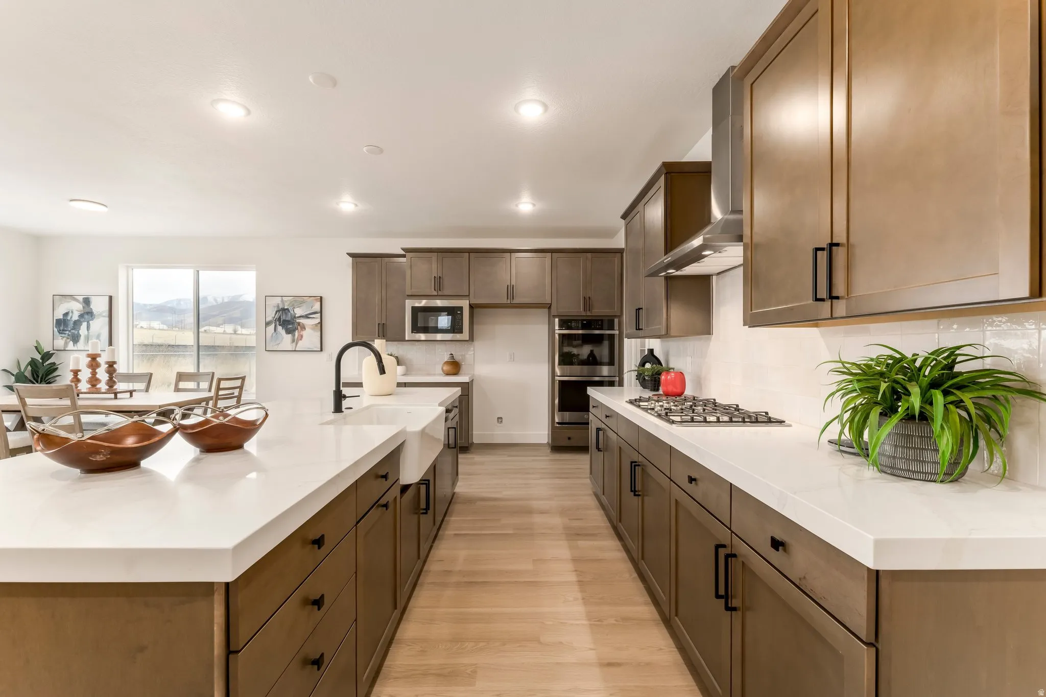 Kitchen with a spacious island, light stone counters, light wood-style flooring, stainless steel appliances, and decorative backsplash