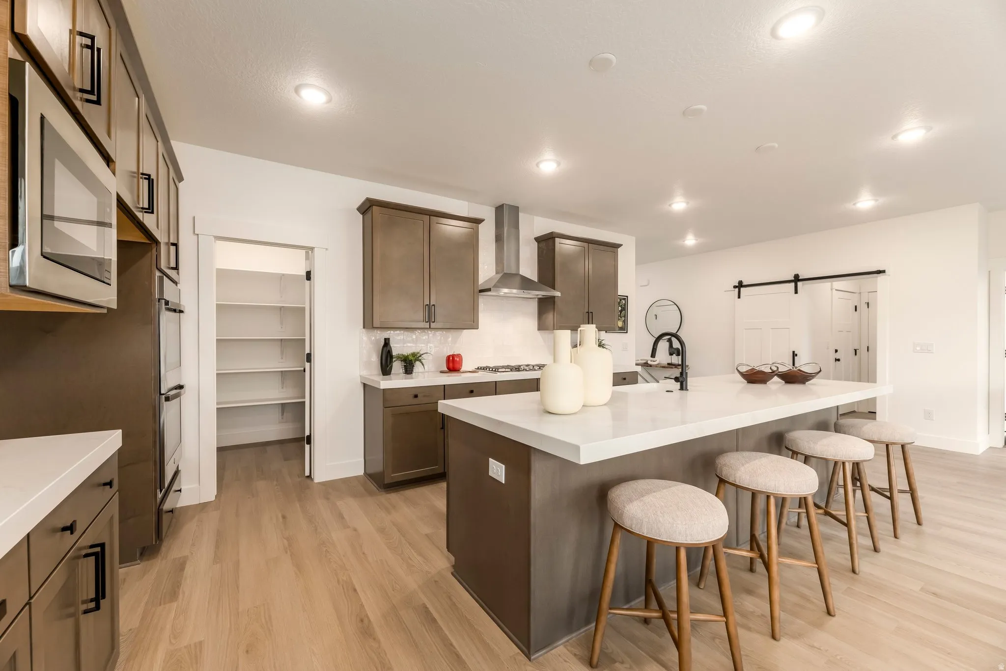 Kitchen featuring a barn door, a kitchen island with sink, light wood-style flooring, decorative backsplash, and stainless steel appliances
