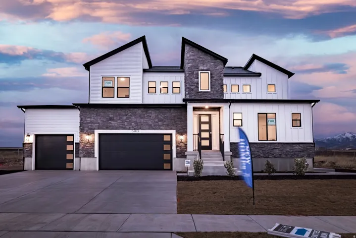 View of front facade featuring board and batten siding, stone siding, driveway, and a garage