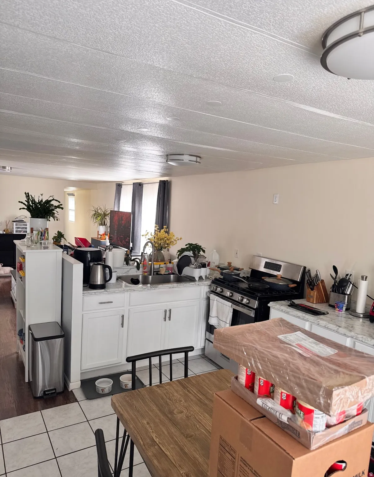 Kitchen with white cabinets, stainless steel gas range, open floor plan, light tile patterned floors, and light stone counters