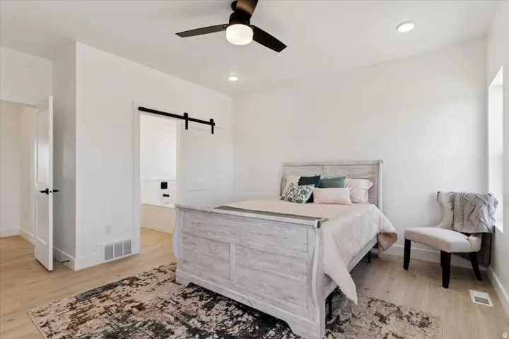 Bedroom with a barn door, light wood-style flooring, and a ceiling fan