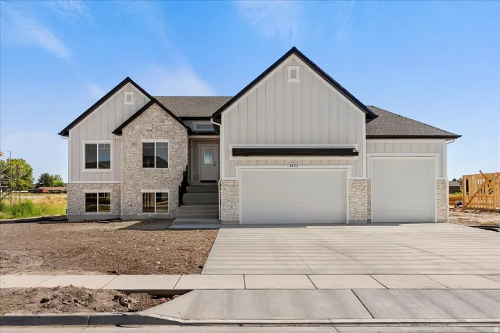 View of front of house with stone siding, board and batten siding, driveway, an attached garage, and a shingled roof