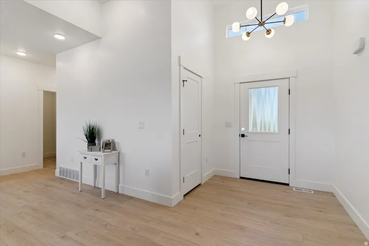 Foyer entrance featuring a chandelier, light wood-style floors, and a towering ceiling