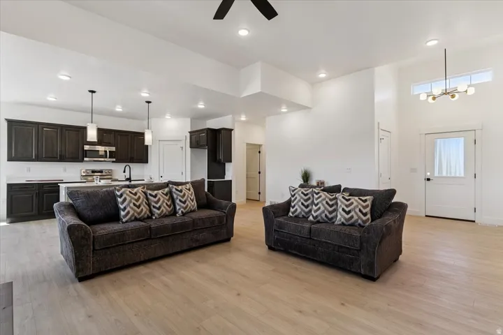 Living area featuring light wood-type flooring, a ceiling fan, a chandelier, recessed lighting, and a towering ceiling