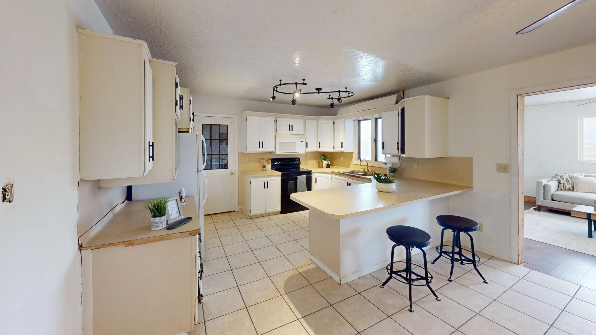 Kitchen featuring light countertops, black range with electric stovetop, a textured ceiling, a peninsula, and a kitchen bar