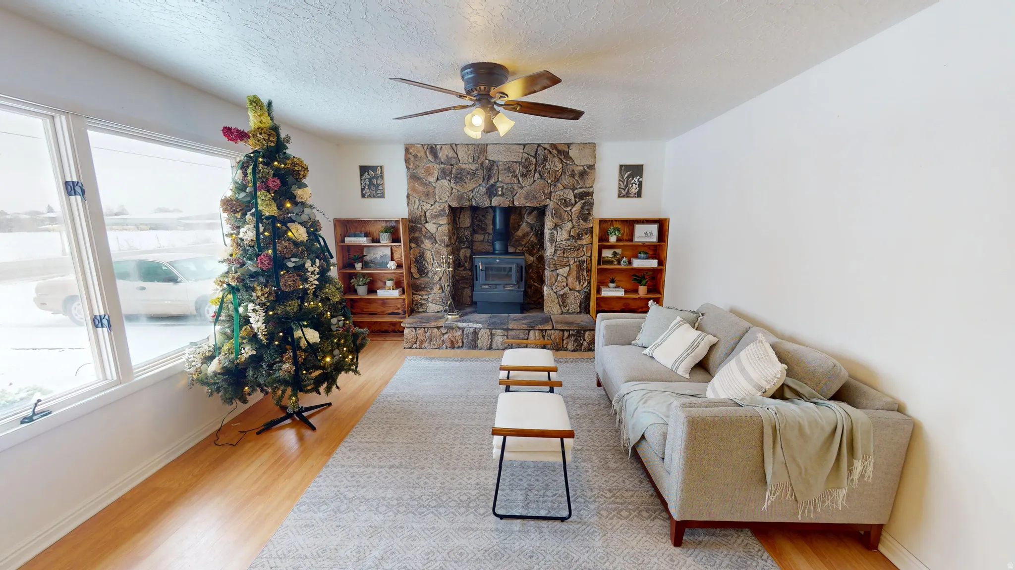 Living area with a wood stove, wood finished floors, a ceiling fan, and a textured ceiling