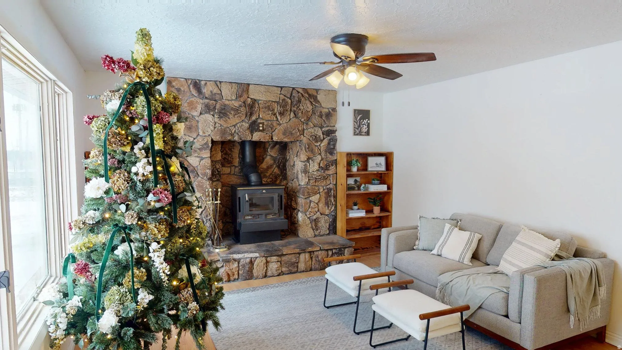Living area featuring a wood stove, wood finished floors, a textured ceiling, and a ceiling fan
