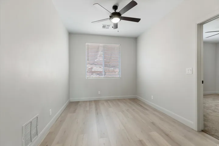 Wood-finish flooring, ceiling fan with integrated lighting, window with horizontal blinds, and neutral wall tones
