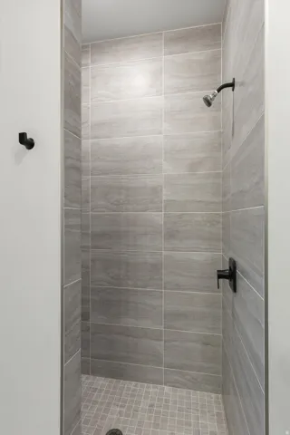 Shower stall featuring large format gray wall tiling, gray mosaic floor tiling, and matte black fixtures