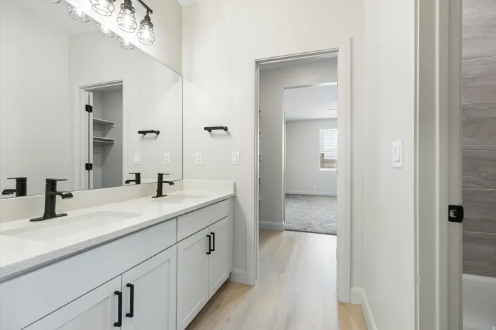 Dual vanity with matte black fixtures, light-toned countertops, contemporary cabinetry, and wood-finish flooring