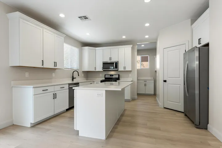 Modern kitchen featuring white shaker cabinetry, stainless steel appliances, a center island, and wood-finish flooring