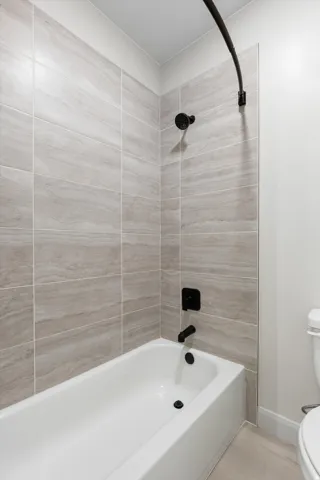 Tub and shower combination featuring tiled surround, matte black fixtures, and a curved shower rod