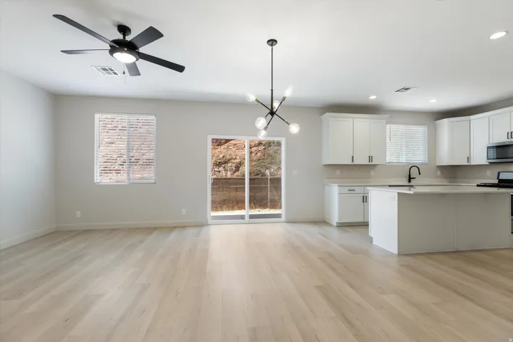 Light wood-finish flooring throughout, modern black ceiling fan, contemporary chandelier, white kitchen cabinetry with dark hardware, and sliding glass door