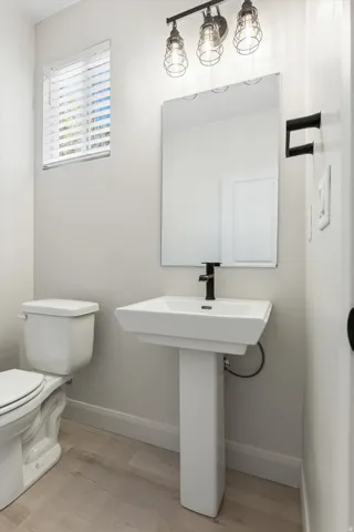 Pedestal sink with a matte black faucet, wall-mounted mirror, and industrial-style vanity lighting