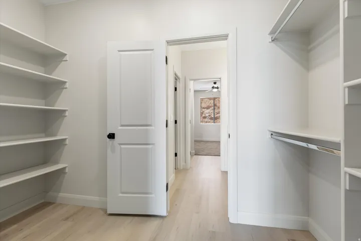 Built-in shelving, white paneled door with black hardware, wood-finish flooring, and closet rods
