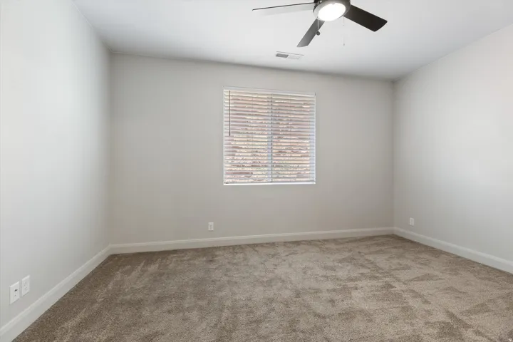 Neutral wall color, window with blinds, overhead ceiling fan with lighting, and plush carpet flooring