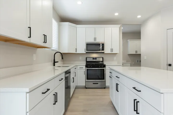 Modern kitchen featuring white cabinetry, light-colored countertops, stainless steel appliances, a kitchen island, and wood-finish flooring
