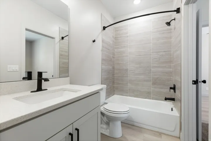 Bathroom featuring a vanity with an integrated sink, black matte fixtures, a tiled tub/shower combination, and wood-finish flooring