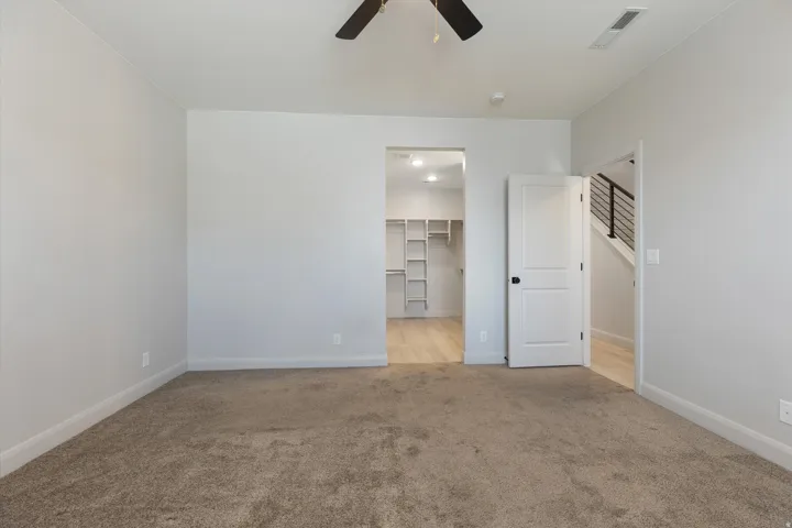 Carpeted room with a ceiling fan, a walk-in closet with built-in shelving, a white paneled door, and wood-finish flooring