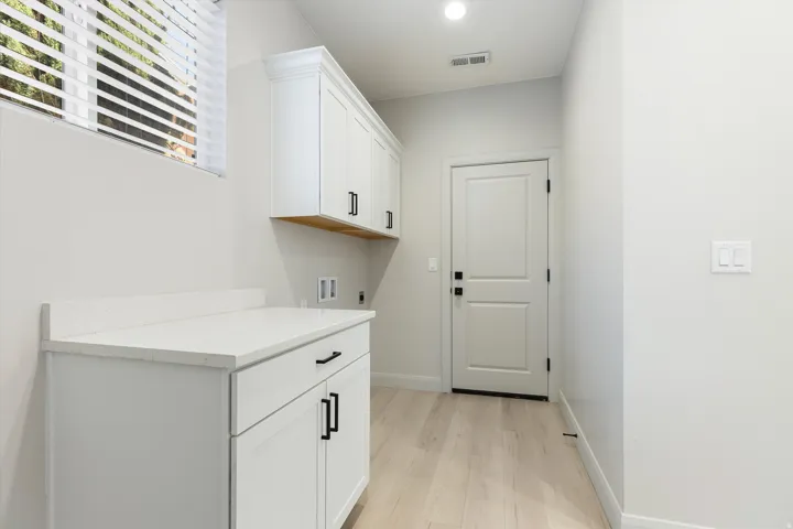 White shaker-style cabinetry with black hardware, white countertop, wood-finish flooring, and recessed ceiling lighting