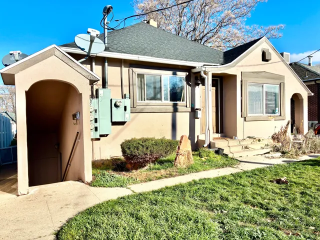 View of front facade with stucco siding, roof with shingles, and a front yard