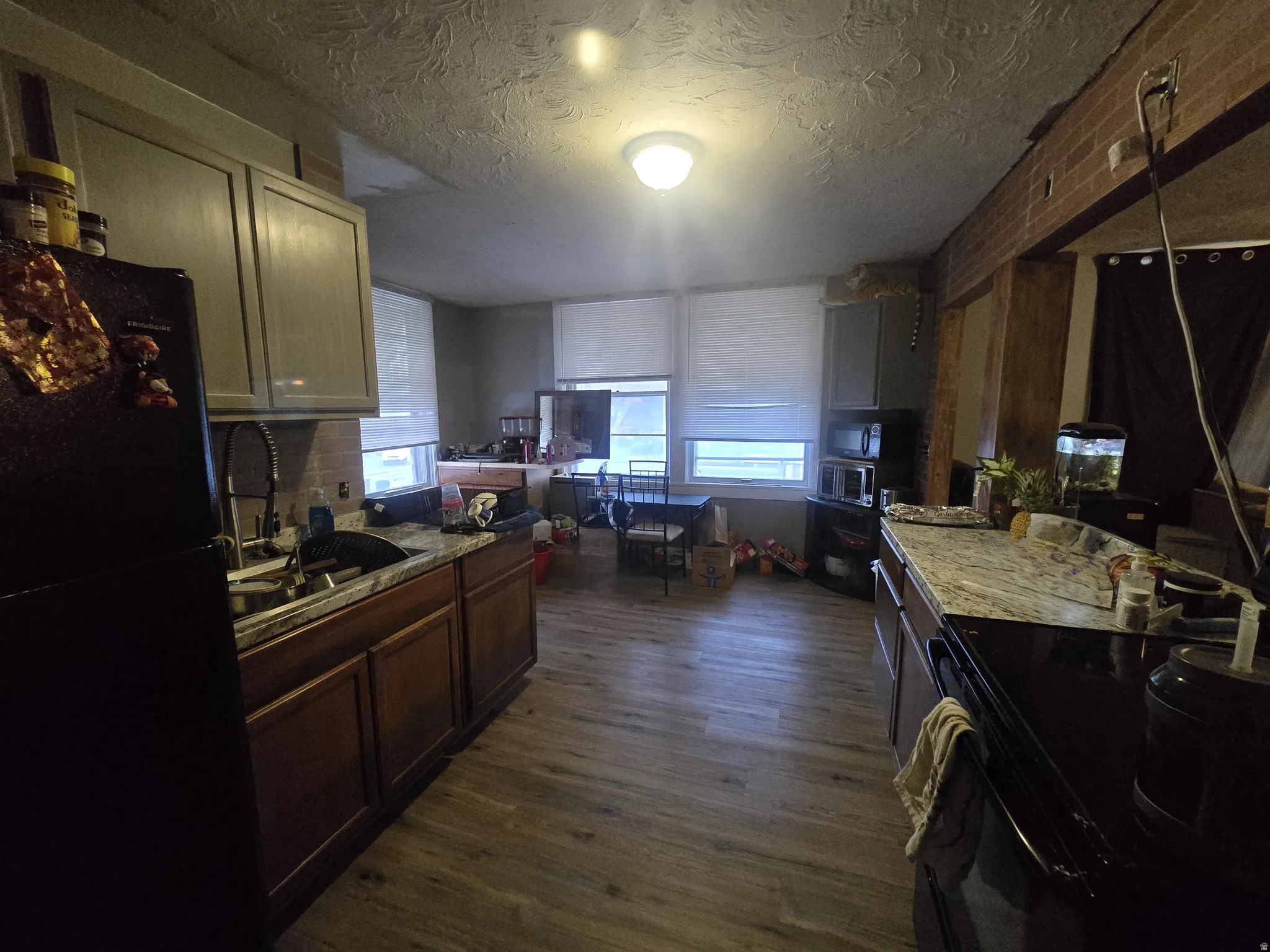Kitchen with freestanding refrigerator, dark wood-style flooring, a textured ceiling, light stone countertops, and open floor plan