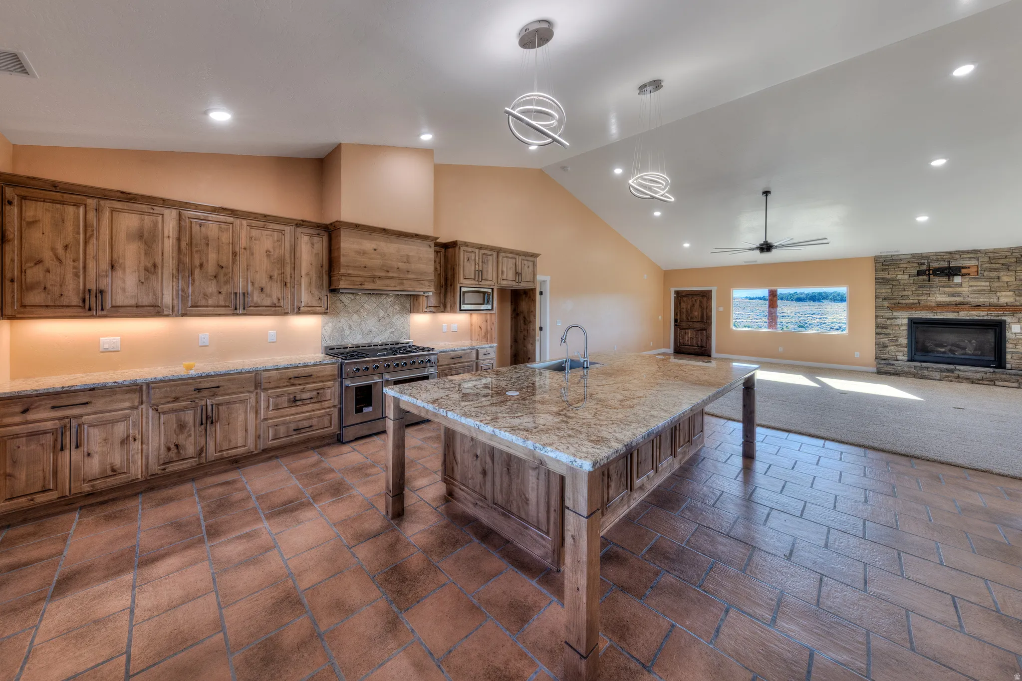 Kitchen featuring brown cabinets, a kitchen island with sink, recessed lighting, a kitchen bar, and high vaulted ceiling