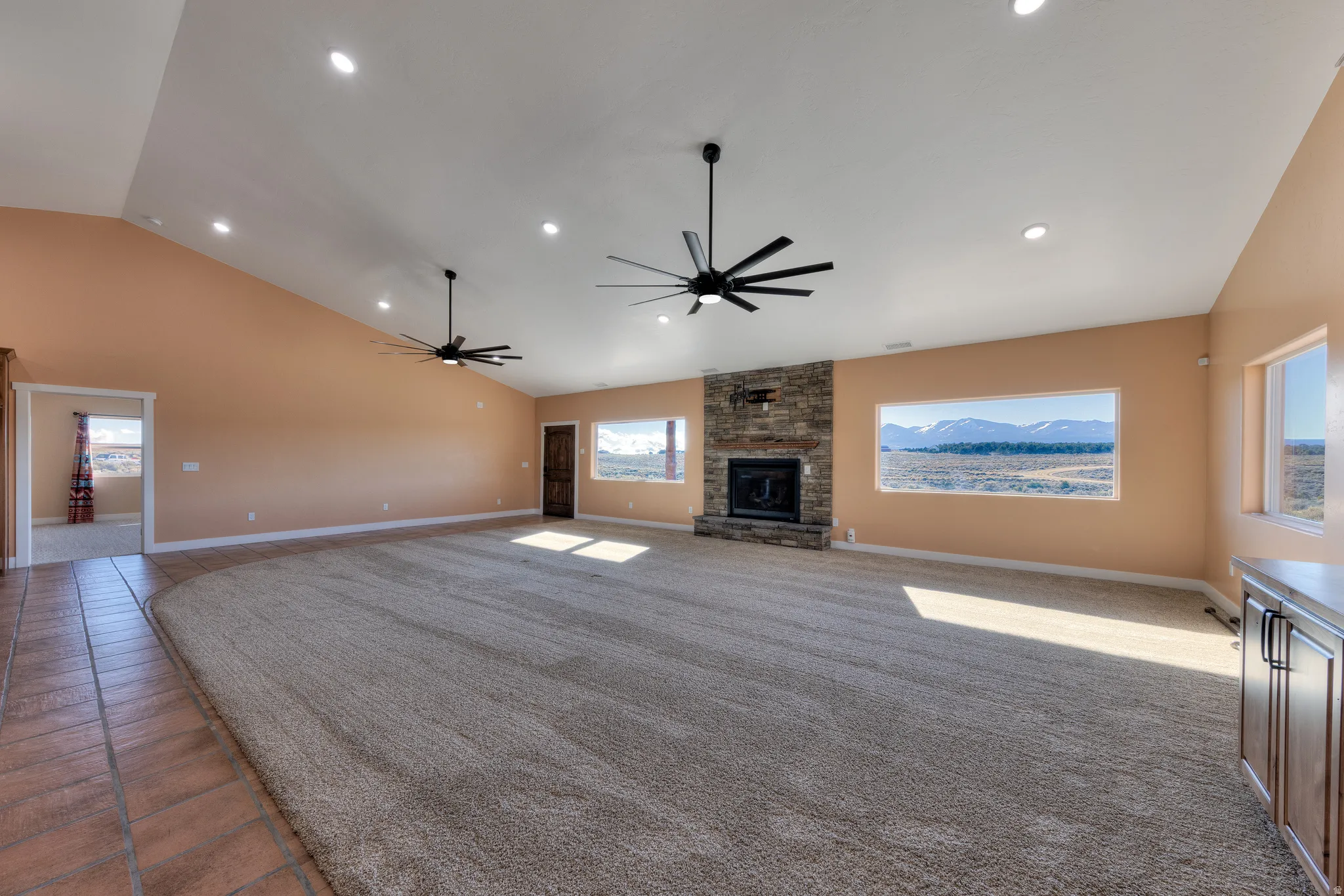Unfurnished living room featuring plenty of natural light, ceiling fan, a stone fireplace, high vaulted ceiling, and carpet flooring