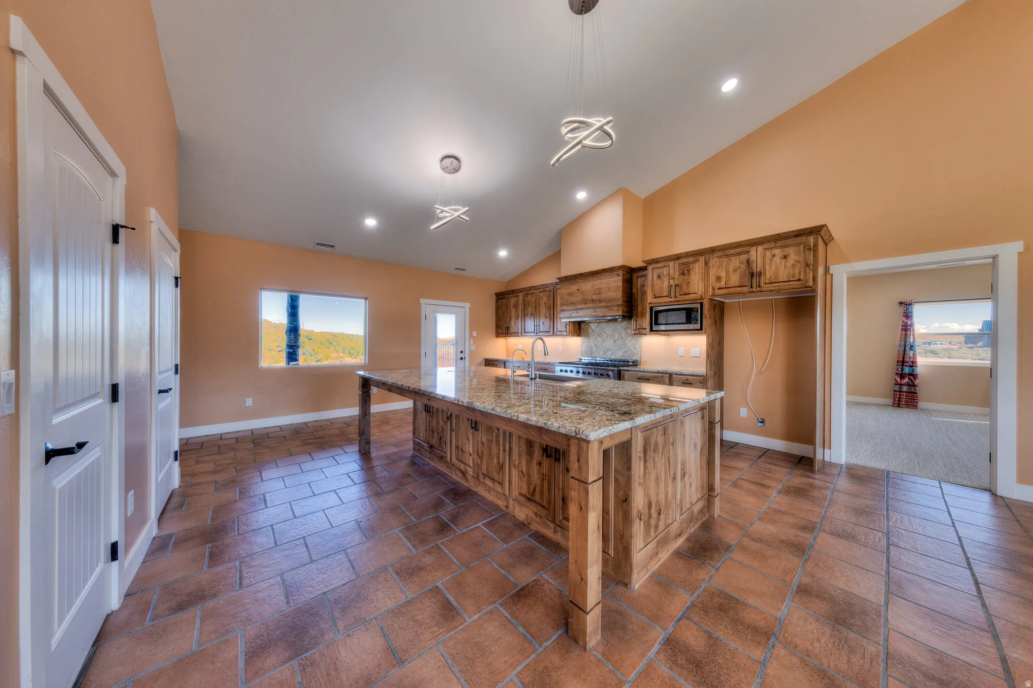 Kitchen featuring a kitchen island with sink, brown cabinets, light stone counters, recessed lighting, and decorative light fixtures