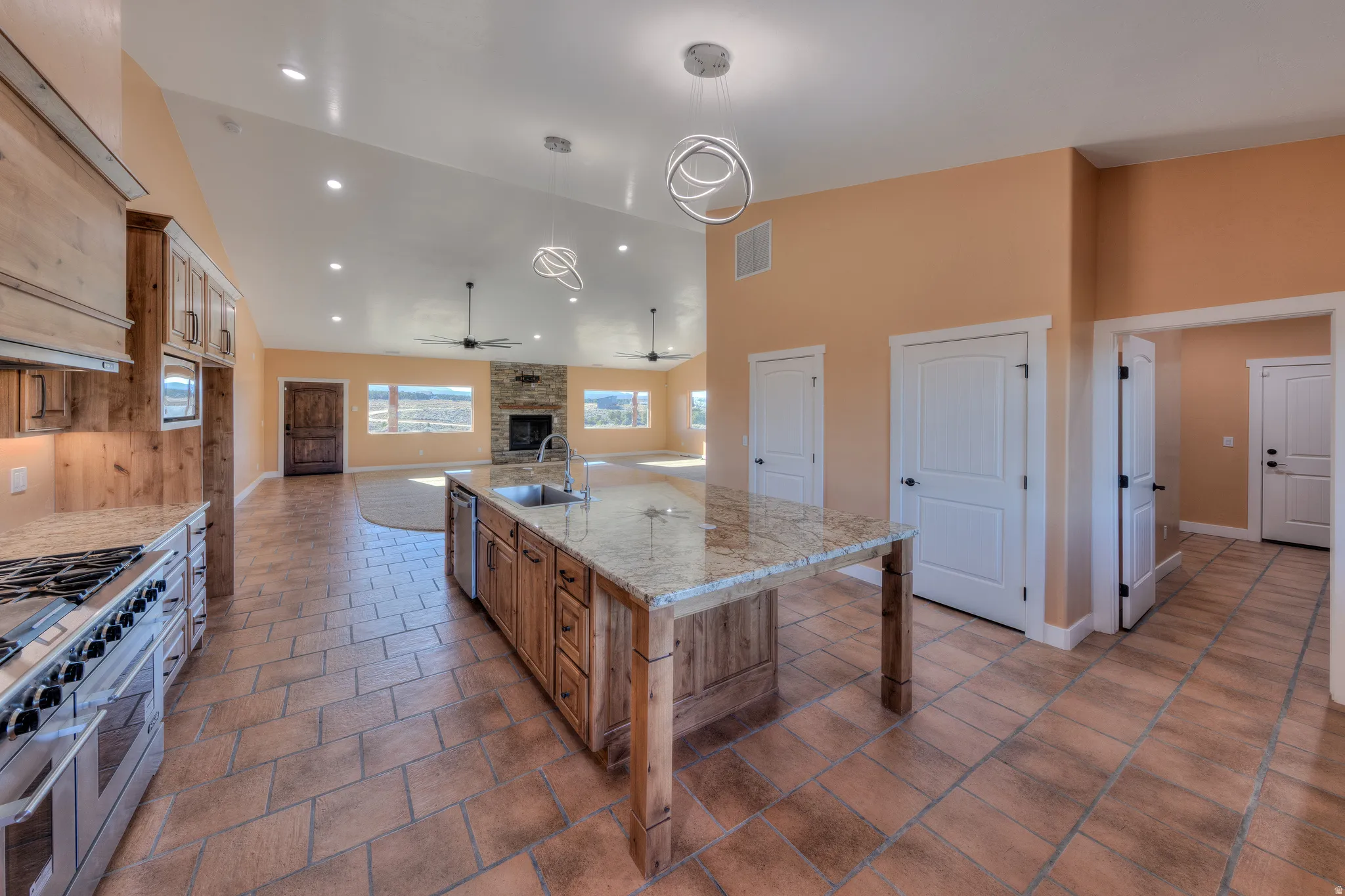 Kitchen with a brick fireplace, a large island, appliances with stainless steel finishes, pendant lighting, and high vaulted ceiling