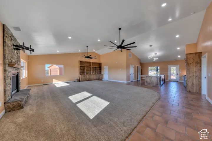 Unfurnished living room with a stone fireplace, high vaulted ceiling, a ceiling fan, dark carpet, and recessed lighting