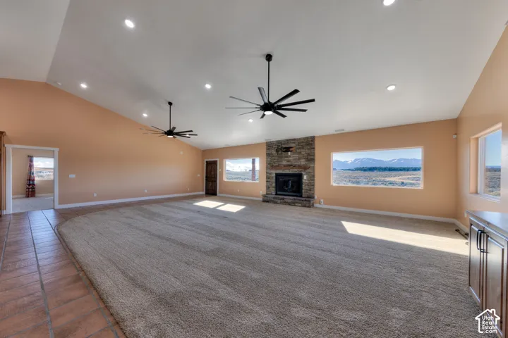 Unfurnished living room featuring plenty of natural light, ceiling fan, a stone fireplace, high vaulted ceiling, and carpet flooring
