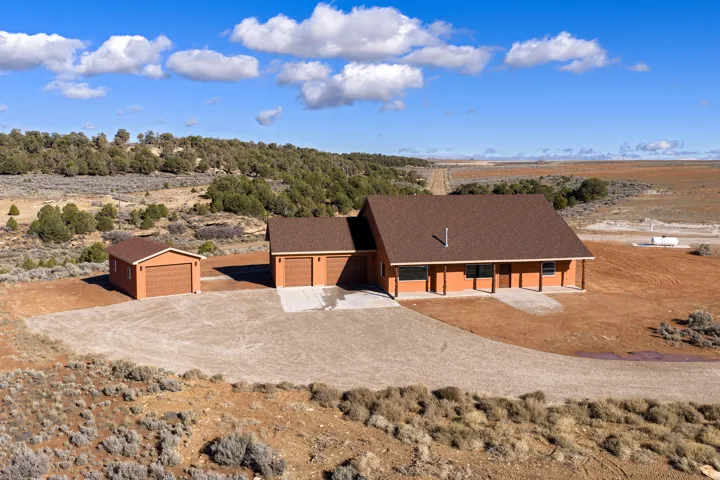 View of front facade with roof with shingles, driveway, a garage, and view of desert landscape