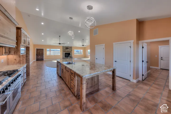 Kitchen with a brick fireplace, a large island, appliances with stainless steel finishes, pendant lighting, and high vaulted ceiling