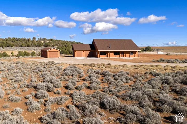 Rear view of property featuring an outdoor structure, a shingled roof, driveway, and a view of rural / pastoral area