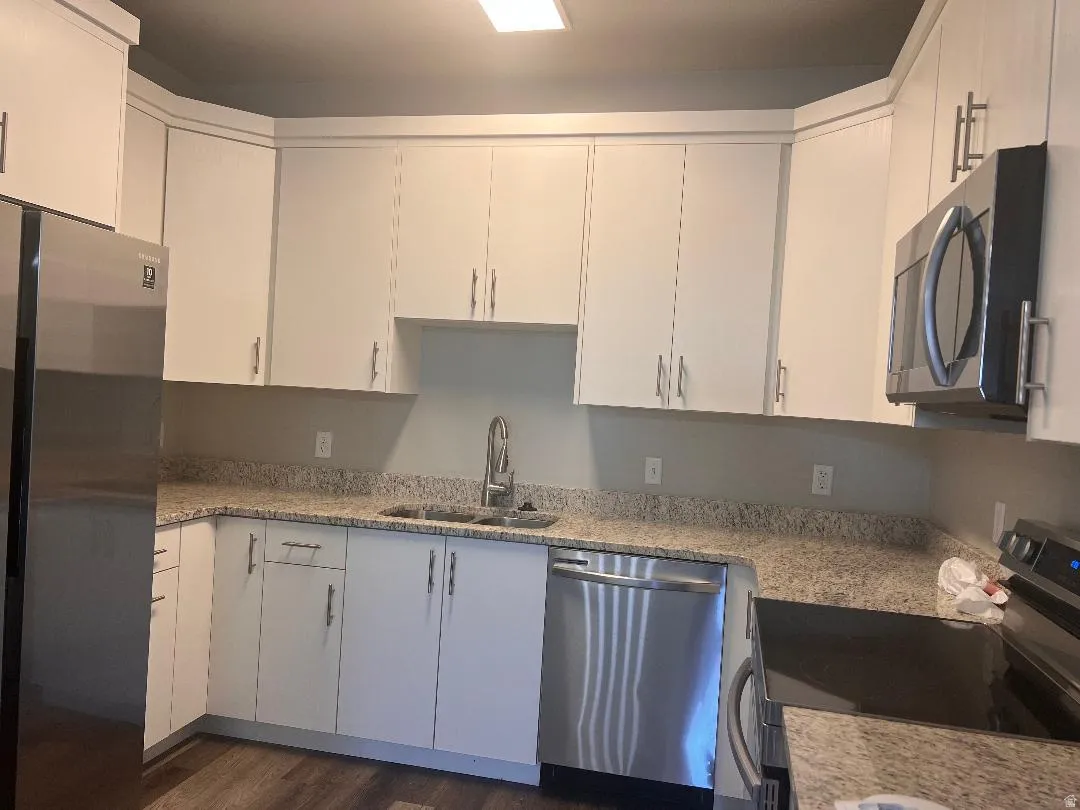 Kitchen with appliances with stainless steel finishes, white cabinets, light stone countertops, and dark wood-style floors