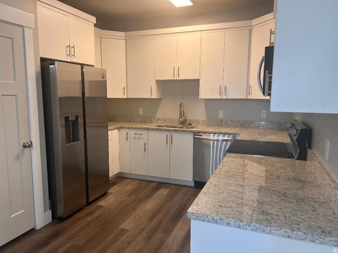 Kitchen with appliances with stainless steel finishes, white cabinets, light stone countertops, and dark wood-type flooring