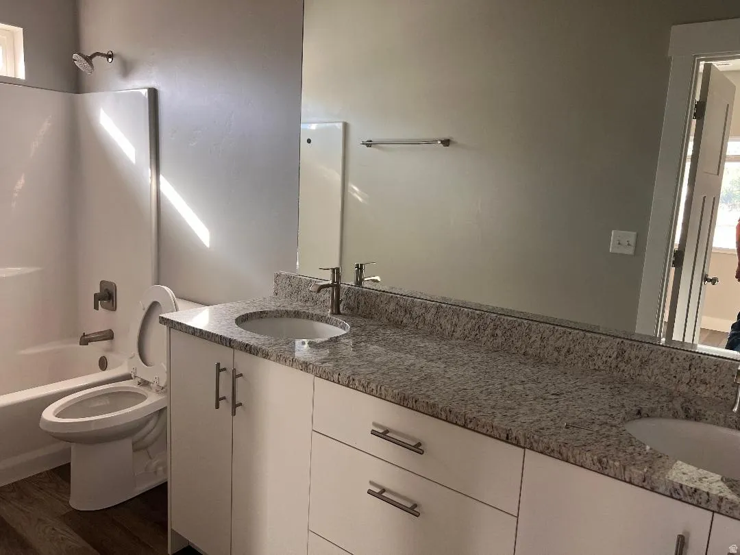 Bathroom featuring shower / bath combination, double vanity, and dark wood finished floors