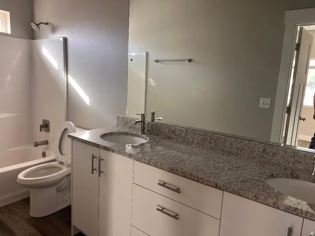 Bathroom featuring shower / bath combination, double vanity, and dark wood finished floors