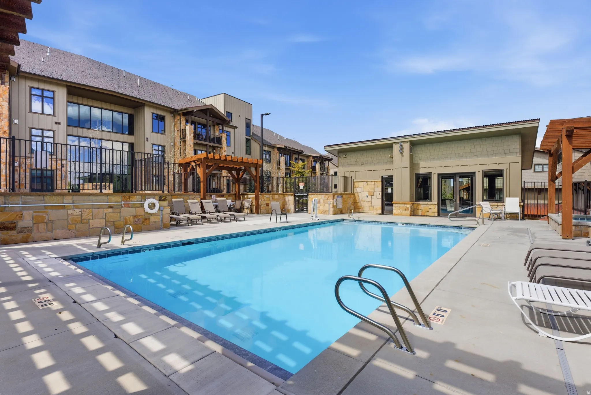 Outdoor swimming pool featuring a perimeter concrete deck, integrated steps, and stainless steel handrails