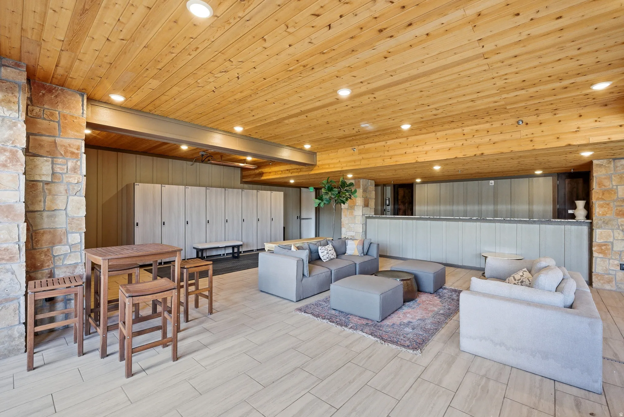 Spacious communal area featuring a wood-panel ceiling, stone accent walls, recessed lighting, and large format tile flooring