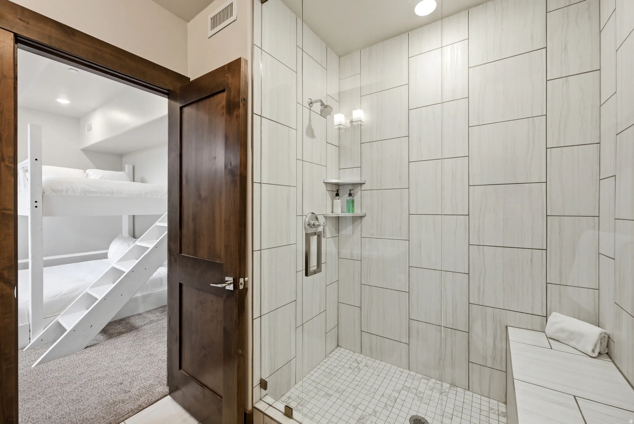 Spacious shower enclosure with floor-to-ceiling tile, built-in bench, and glass panel door