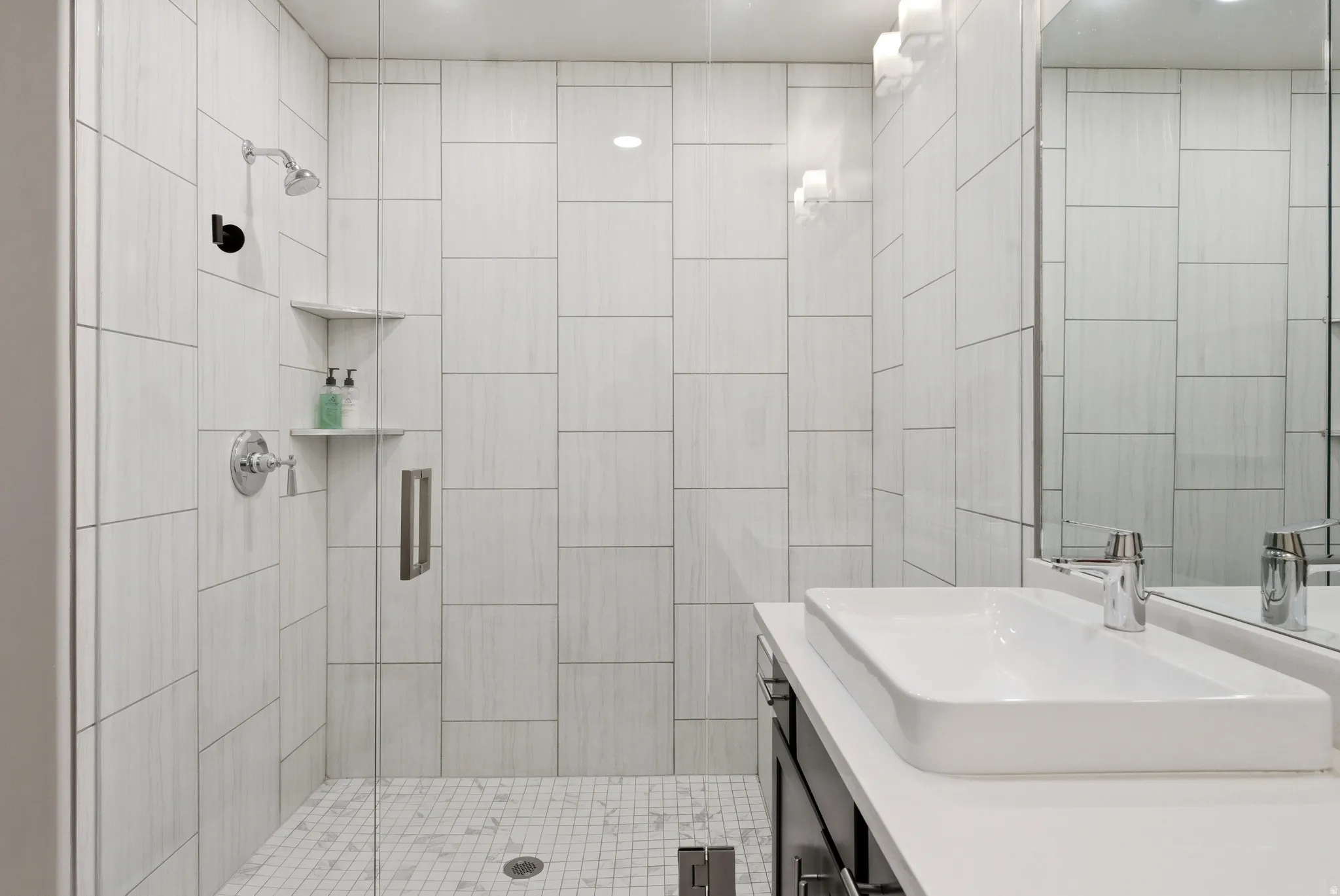 Contemporary bathroom featuring a frameless glass shower enclosure, white subway tile shower surround, and a white rectangular vessel sink with a chrome faucet