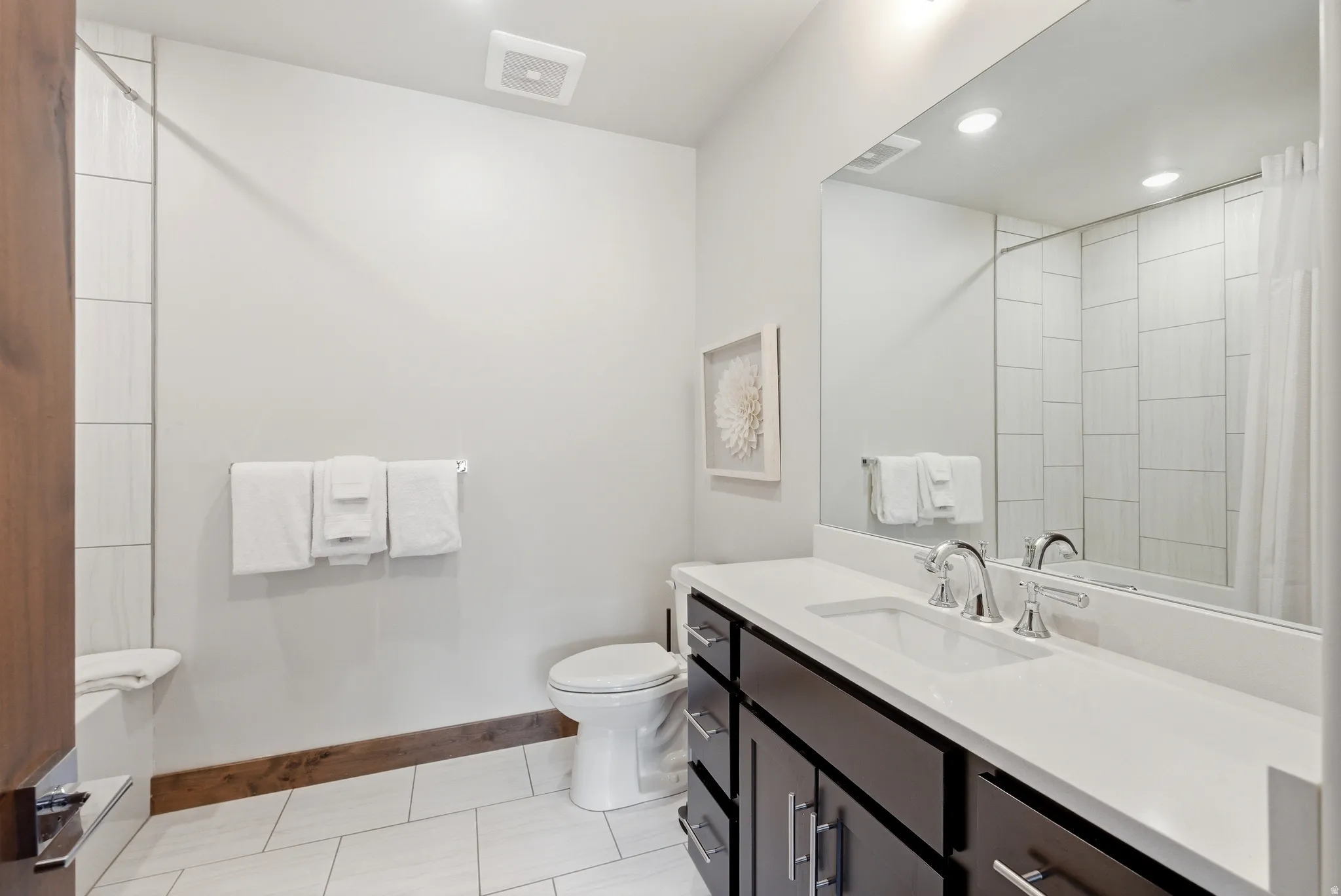 Bathroom featuring a dark wood-finish vanity with a white countertop and integrated sink, chrome faucet, and expansive wall-mounted mirror
