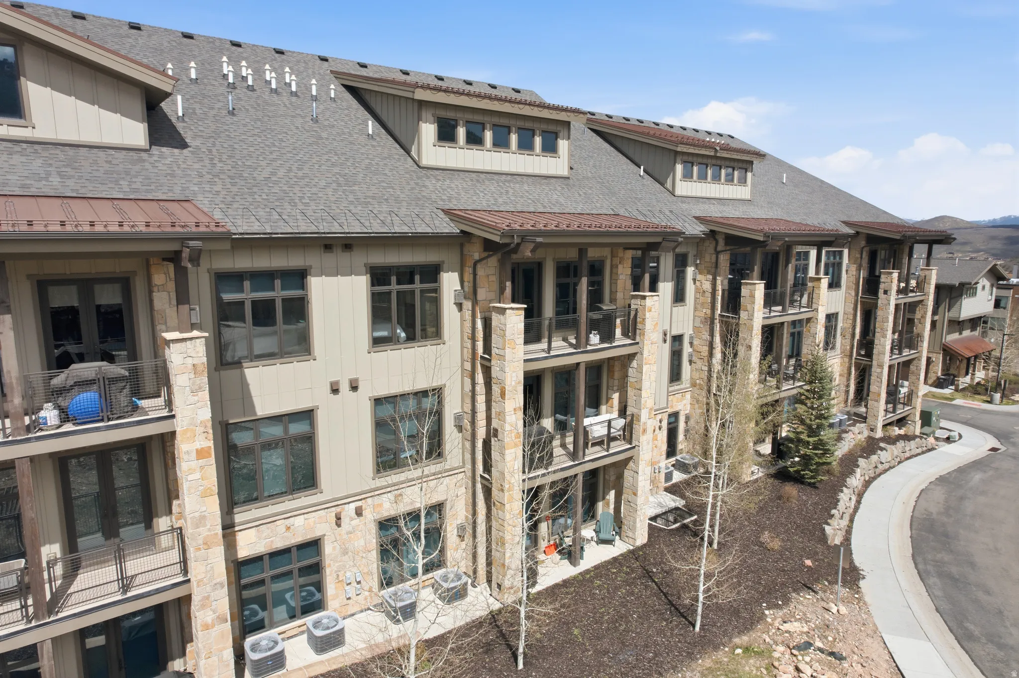 Multi-story building featuring stone and siding exterior, multiple balconies, a covered entry, and dormer windows
