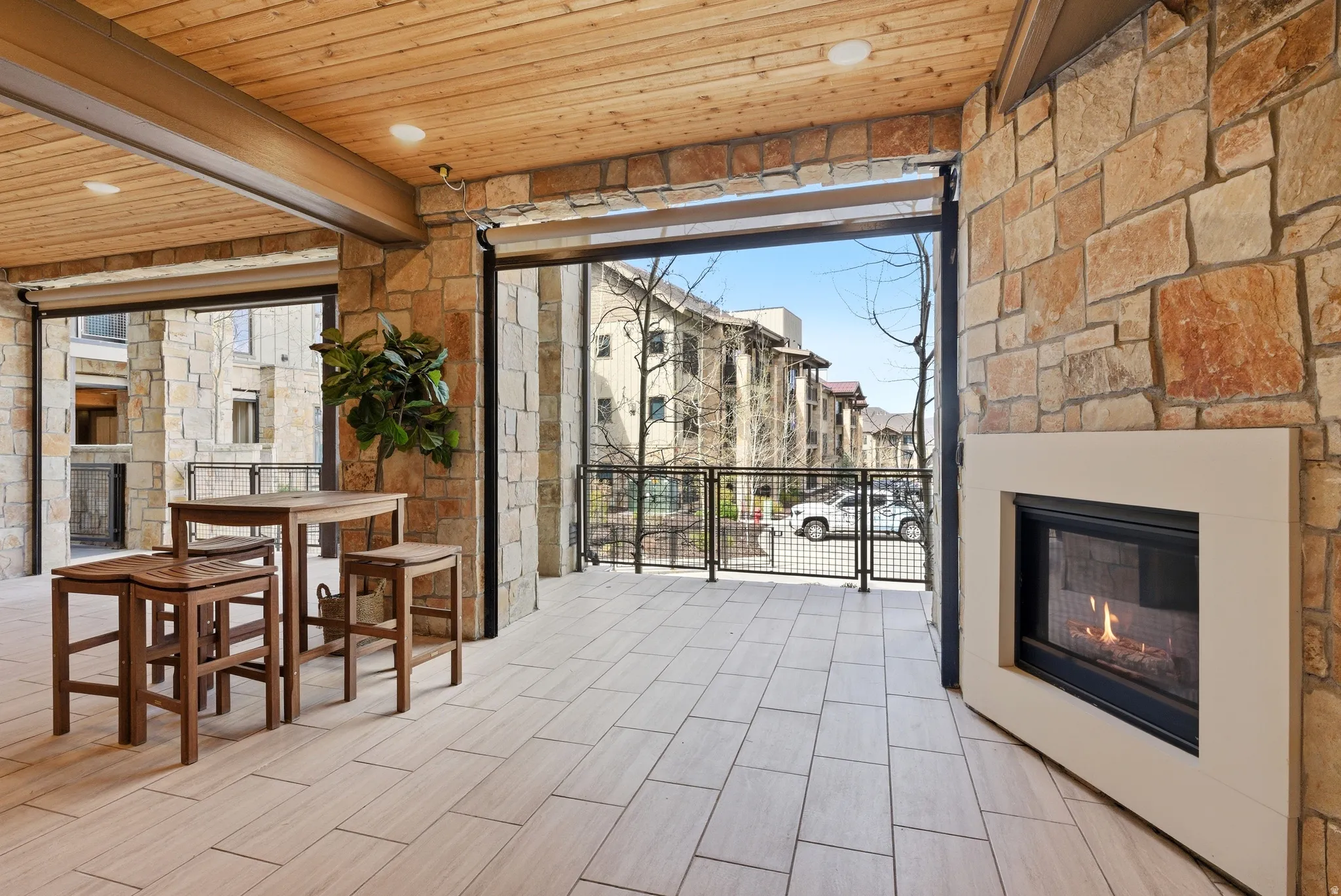 Covered outdoor living space featuring stone walls, a wood-paneled ceiling, and light-colored tile flooring